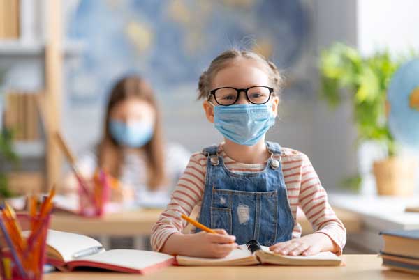 An Schulen werden noch Masken getragen. Ein Kind sitzt mit Maske in der Schule.